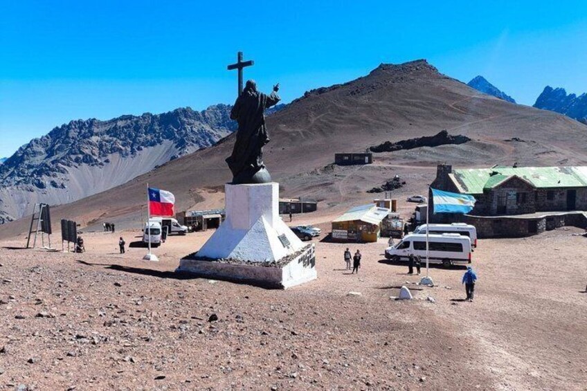 A statue on a pedestal, a flag, a building, and a mountainous landscape. 2