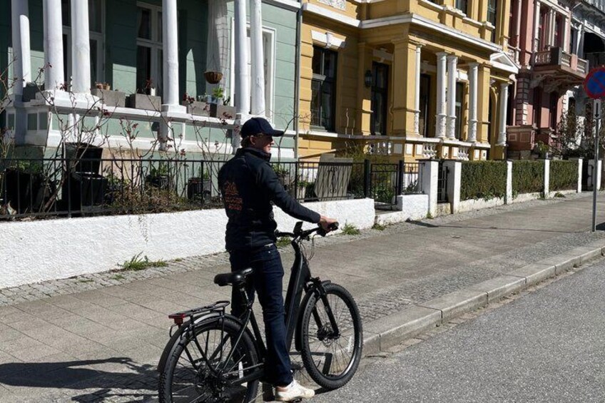A person standing next to a bicycle on a sidewalk in front of a row of colorful buildings. 4