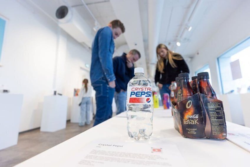 A table with Crystal Pepsi, Coca-Cola Blak, and a bottle of water in a modern indoor setting. 2
