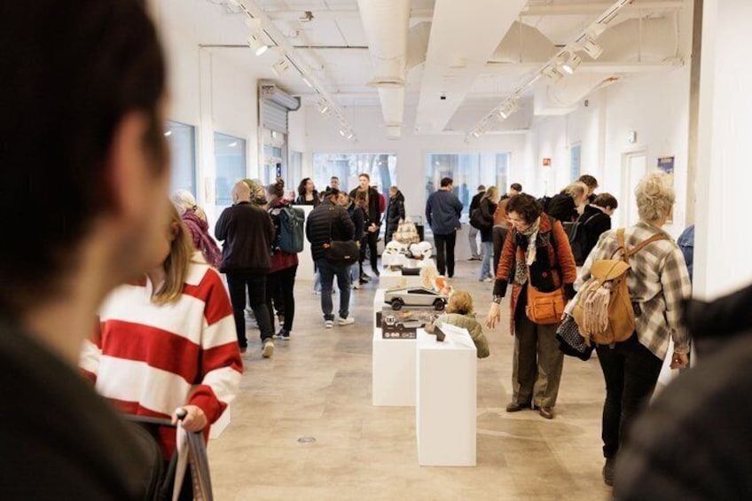 A spacious indoor art gallery with visitors walking and viewing exhibits. 1