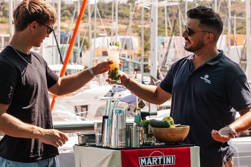 Two men toasting with drinks at a bar with a Martini logo, surrounded by boats and a marina. 3