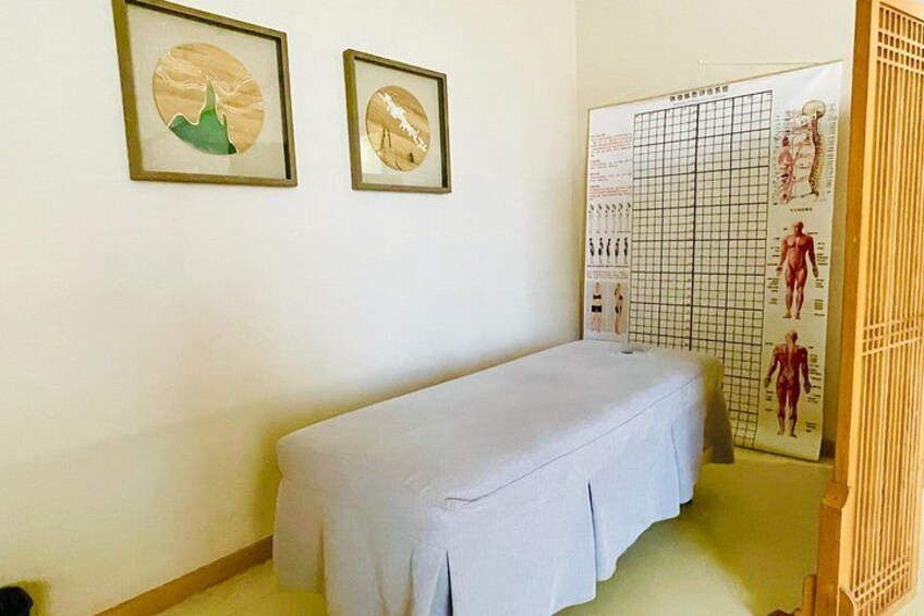 A room with a massage table, framed artwork, and a poster with anatomical illustrations. 5