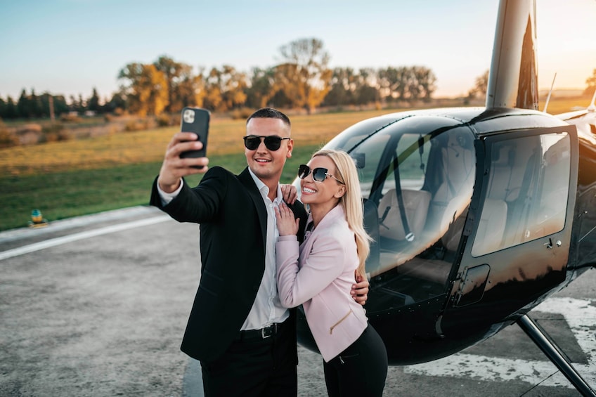 Pariskunta ottaa selfien helikopterin edessä lentokentän kiitotiellä. 1