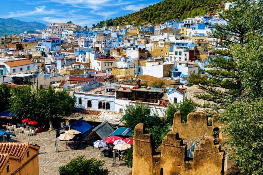 A town with colorful buildings, a castle-like structure, and a mountainous backdrop. 1