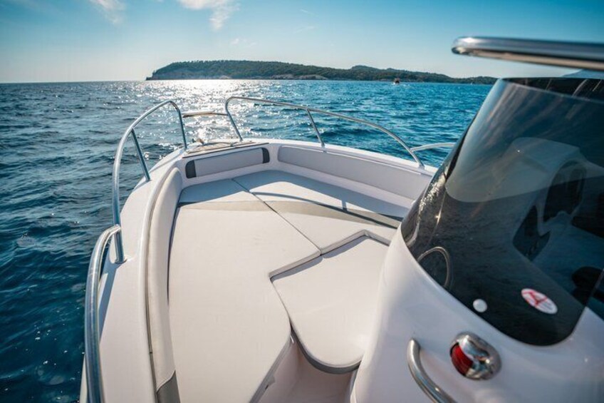 A boat's interior with a white cushioned seating area, metal railings, and a steering wheel. 5