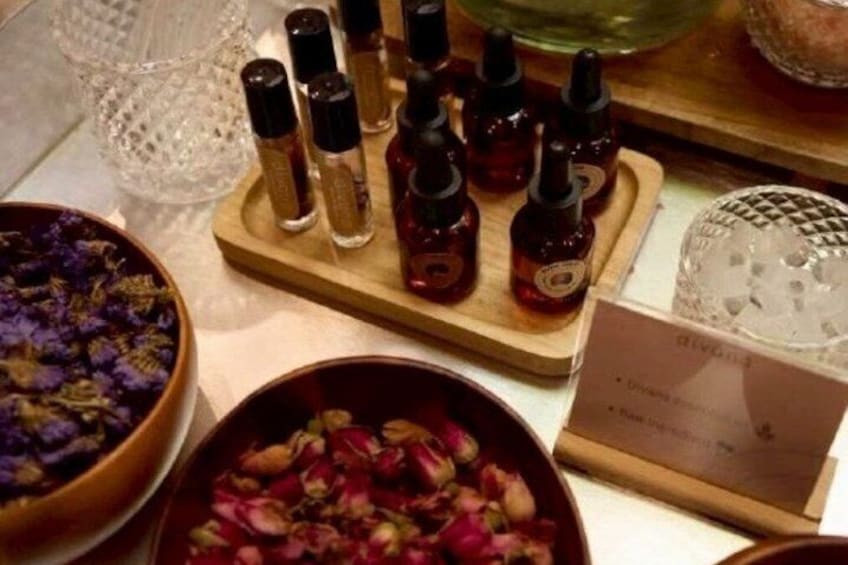 A display of essential oils with bottles on a wooden board, surrounded by bowls of dried flowers. 4