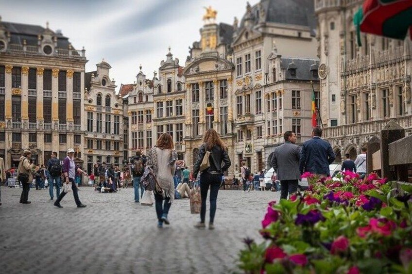 A cobblestone street with historic buildings, pedestrians, and flowers. 4