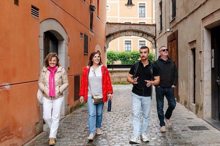 A cobblestone street with buildings, an archway, and a person walking. 1