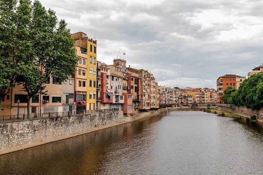 A river with buildings on both sides, a tree on the left, and a cloudy sky. 4