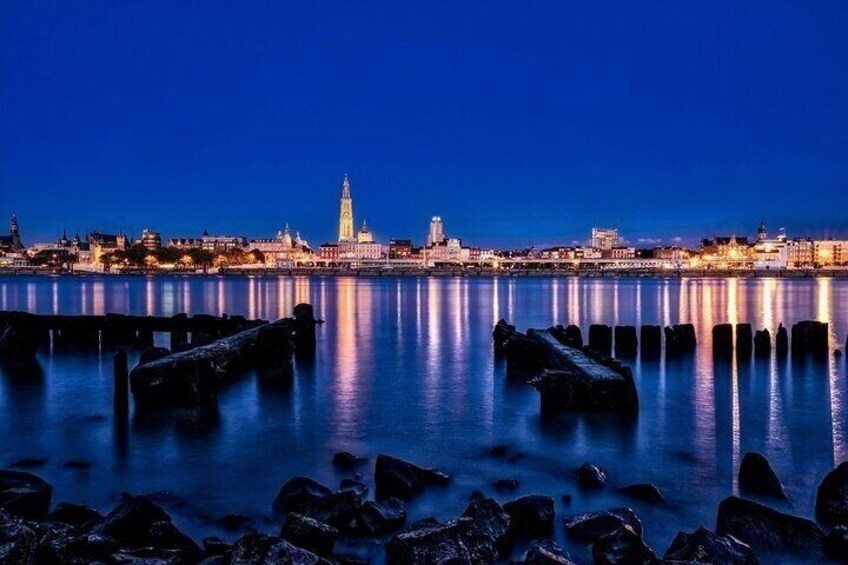 A city skyline at dusk with a prominent tower reflecting on calm water, surrounded by rocky shores. 4