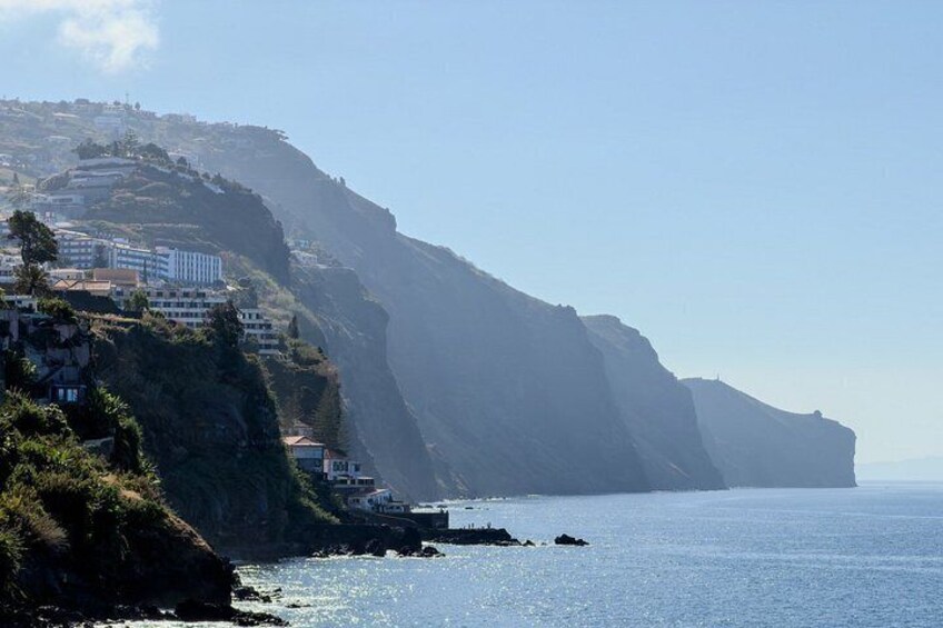 A coastal landscape with a steep cliff, buildings on the hillside, and a calm sea. 2