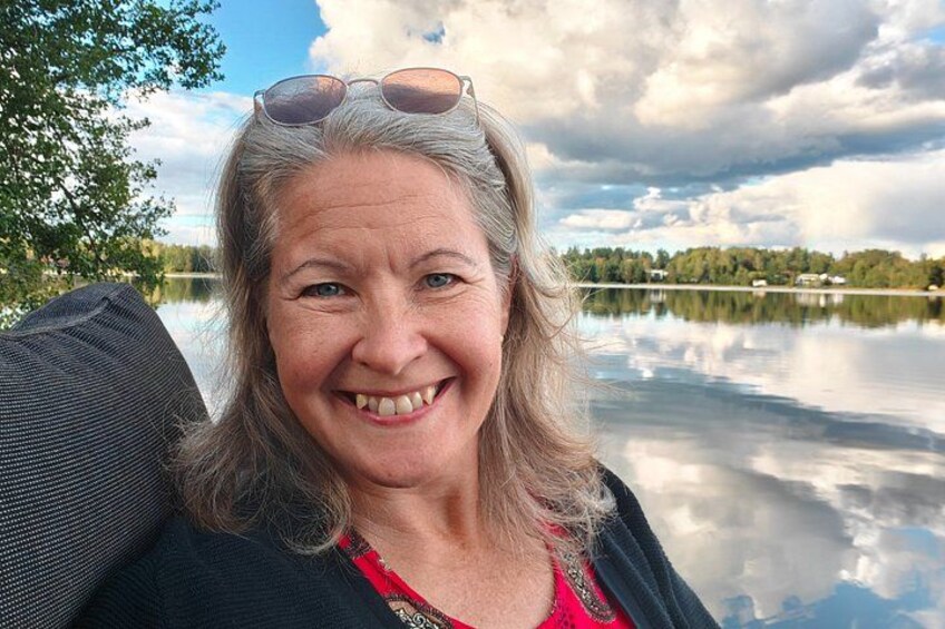 A person sitting by a calm lake with trees and a cloudy sky in the background. 1