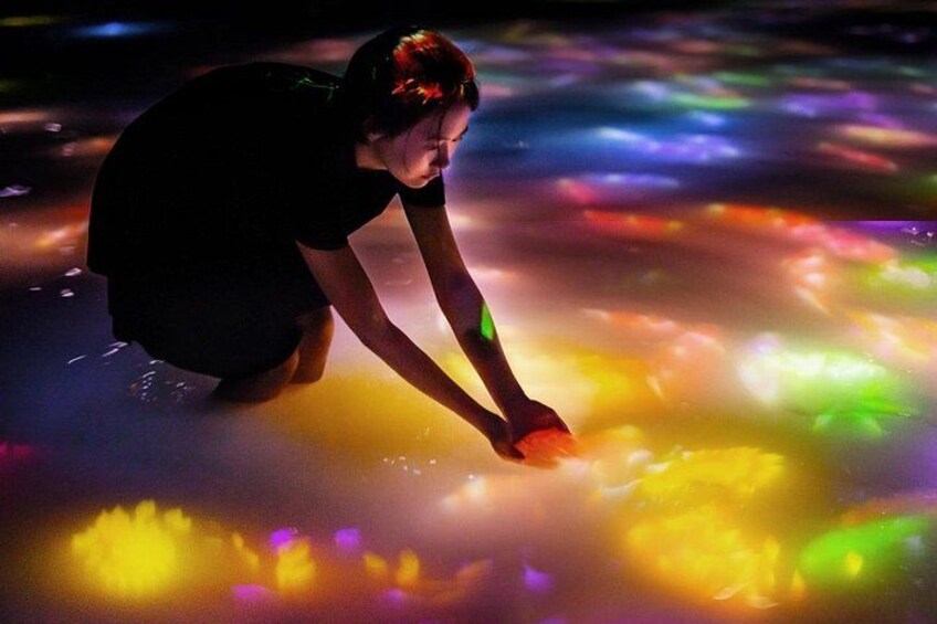 A person interacting with a colorful light installation on the ground. 3