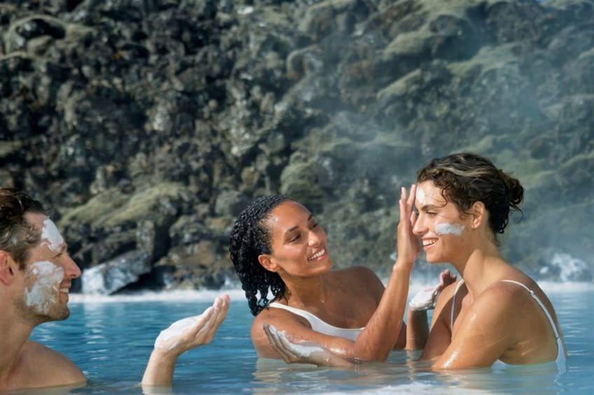 Three people in a hot spring with rocky cliffs in the background. 3