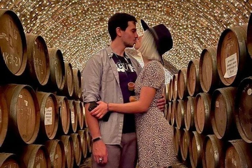 A couple embracing in a wine cellar with rows of wooden barrels. 1