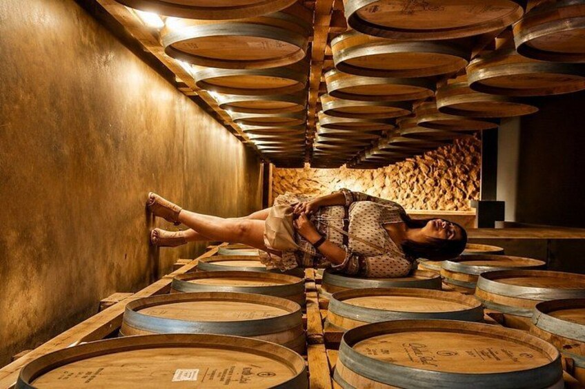 A person lying on wooden barrels in a cellar with wooden walls and barrels stacked on the floor. 3