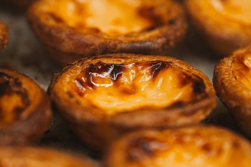A close-up of Portuguese custard tarts with a golden-brown crust and a glossy custard filling. 2