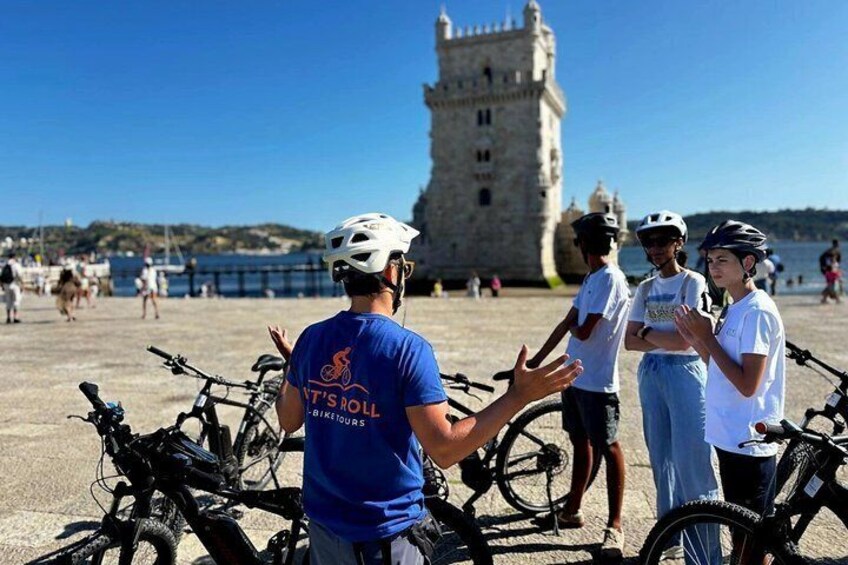 A group of people near bicycles with a historic tower in the background. 1