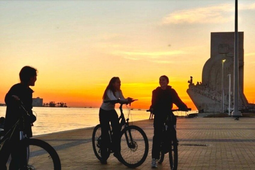 Three people on bicycles by a waterfront during sunset. 3