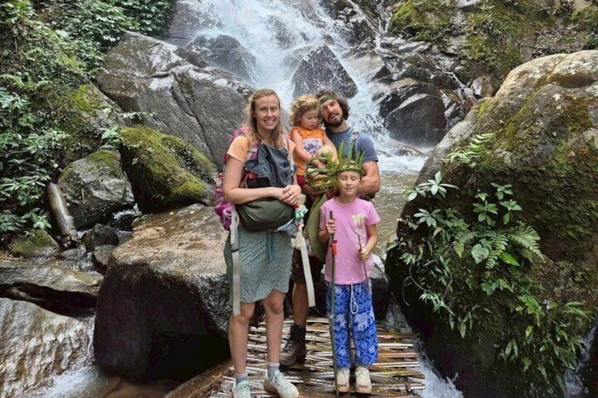 A family standing on a wooden bridge over a waterfall in a forested area. 1