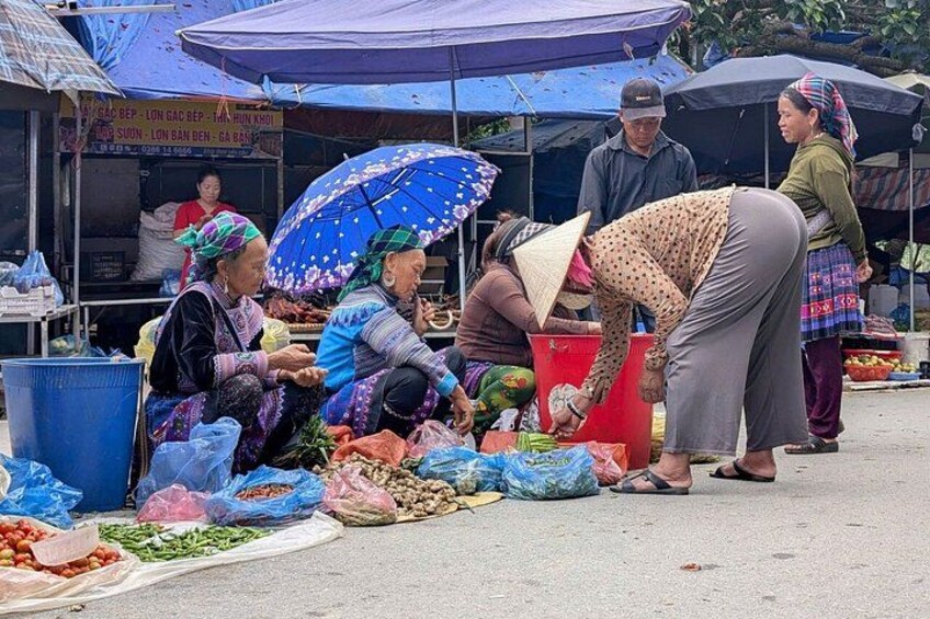 A market scene with people selling and buying goods, covered stalls, and a variety of produce on the ground. 2