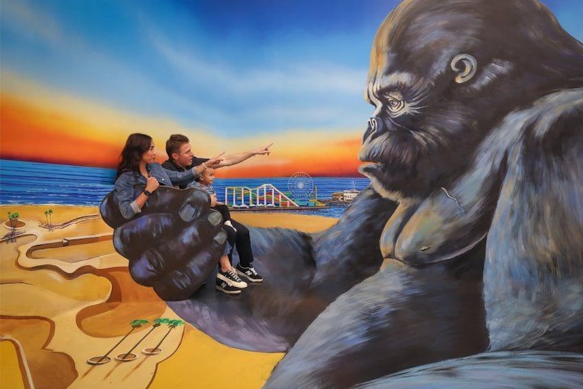 Une fresque représentant un gorille, deux personnes sur une balançoire et un coucher de soleil sur l’eau. 1