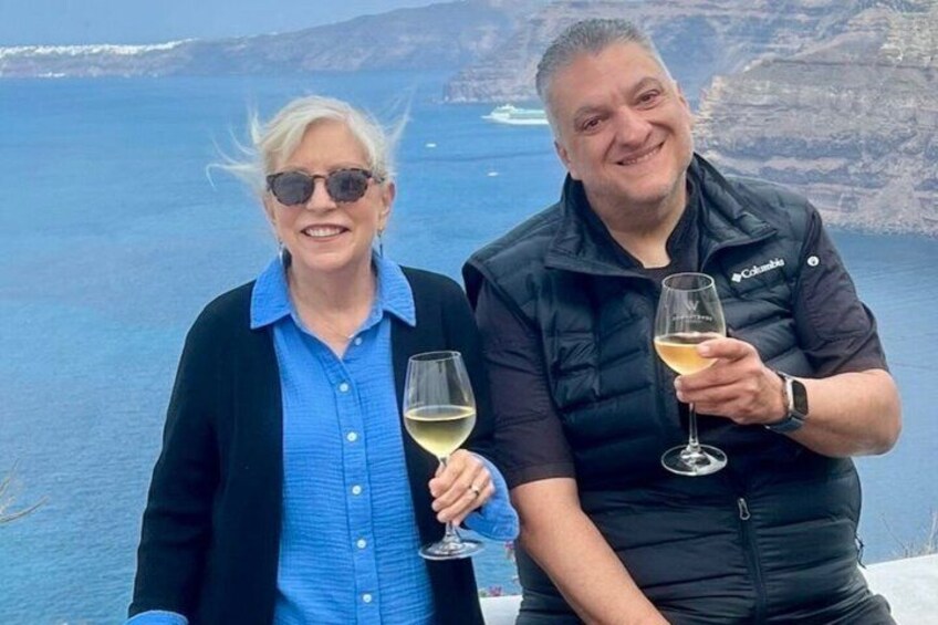 Two people holding wine glasses, overlooking a coastal landscape with cliffs and the sea. 5