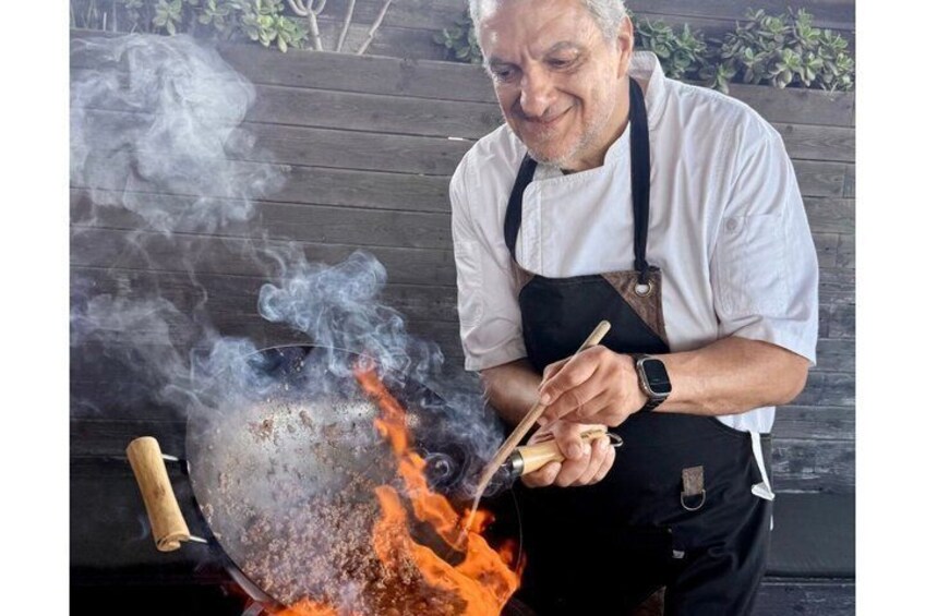 A person cooking with a wok over an open flame, using chopsticks. 1