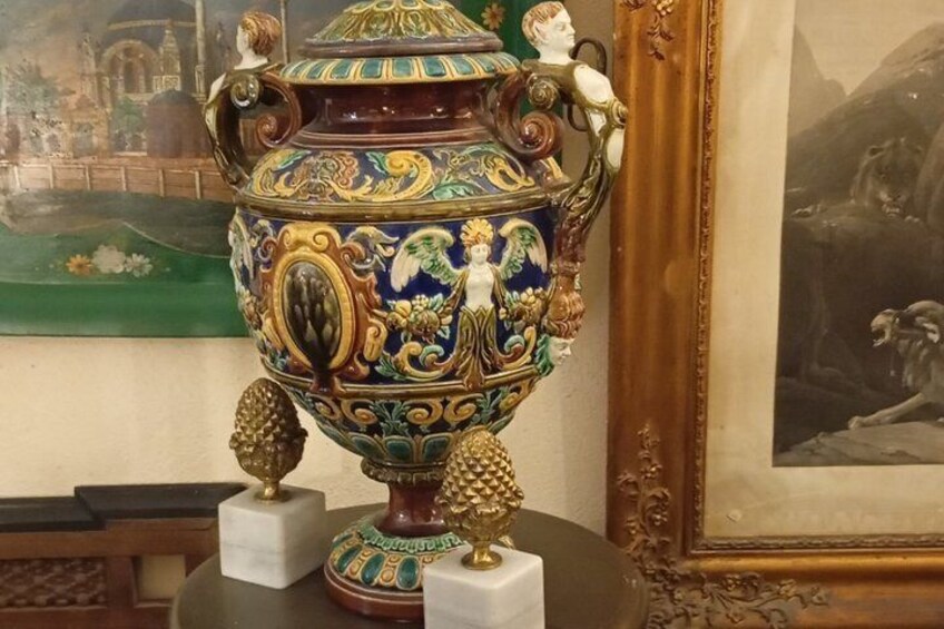 A decorative ceramic urn with intricate designs and two small figurines on pedestals. 5