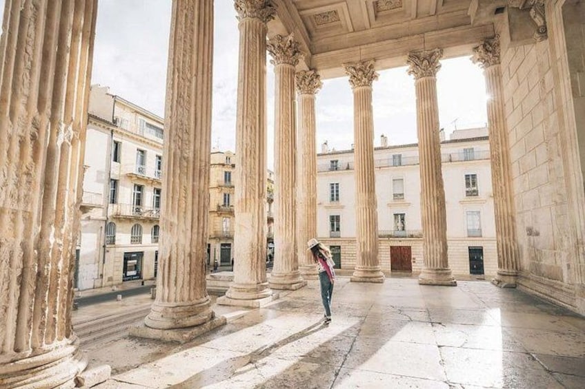 A person standing in a courtyard with classical columns, surrounded by buildings. 1