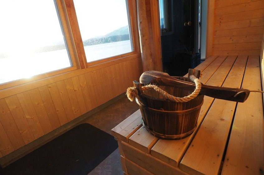 A wooden cabin interior with a wooden bucket on a table, a window with a view of a snowy landscape, and a door. 2