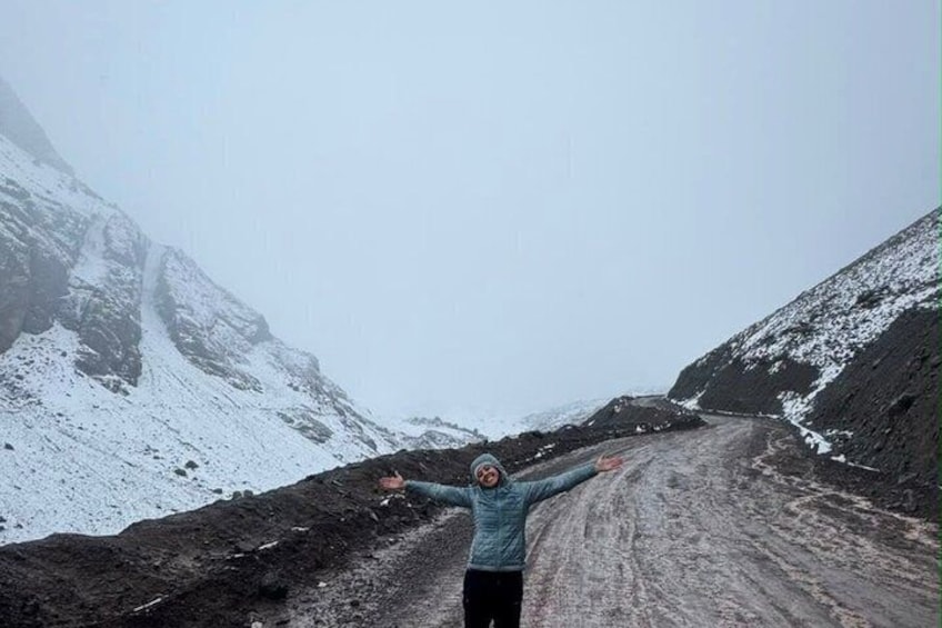 A person standing on a snow-covered road with arms outstretched, surrounded by snow-covered mountains. 2