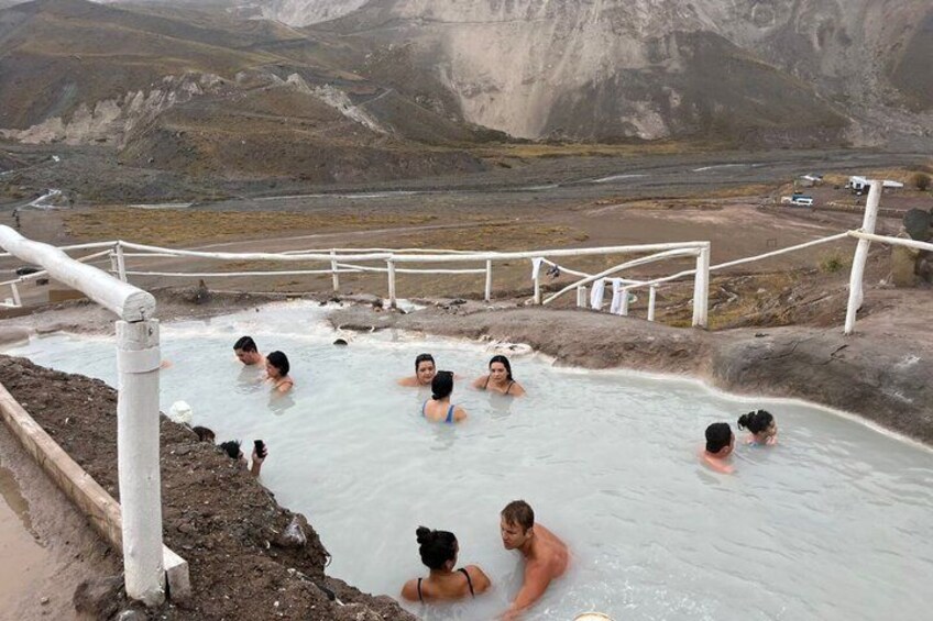 A geothermal hot spring with people swimming, surrounded by a mountainous landscape. 5