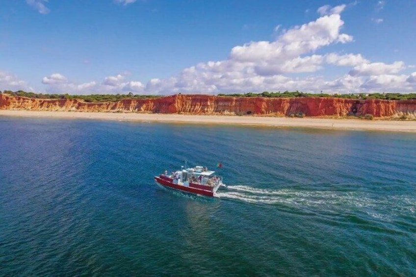 A red boat on a calm sea with a red cliff and clear sky in the background. 1