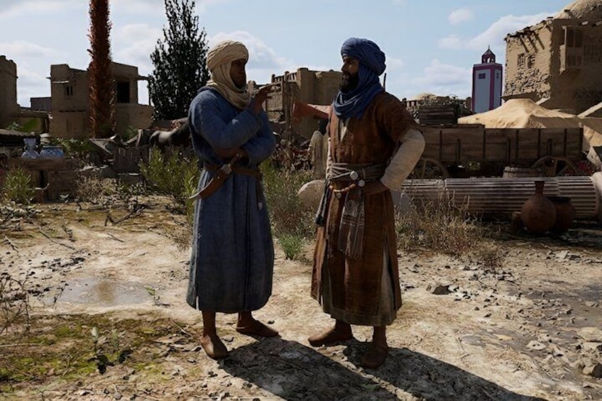Two individuals in traditional attire standing in a desert-like environment with buildings and a palm tree in the background. 2
