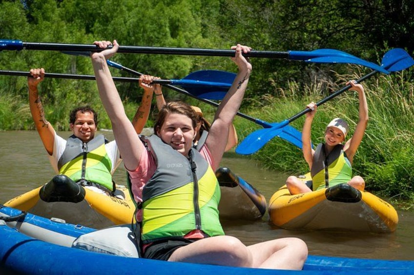 Three people kayaking on a river surrounded by greenery. 4