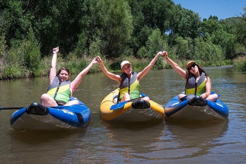 Three people in inflatable rafts on a river surrounded by greenery. 2