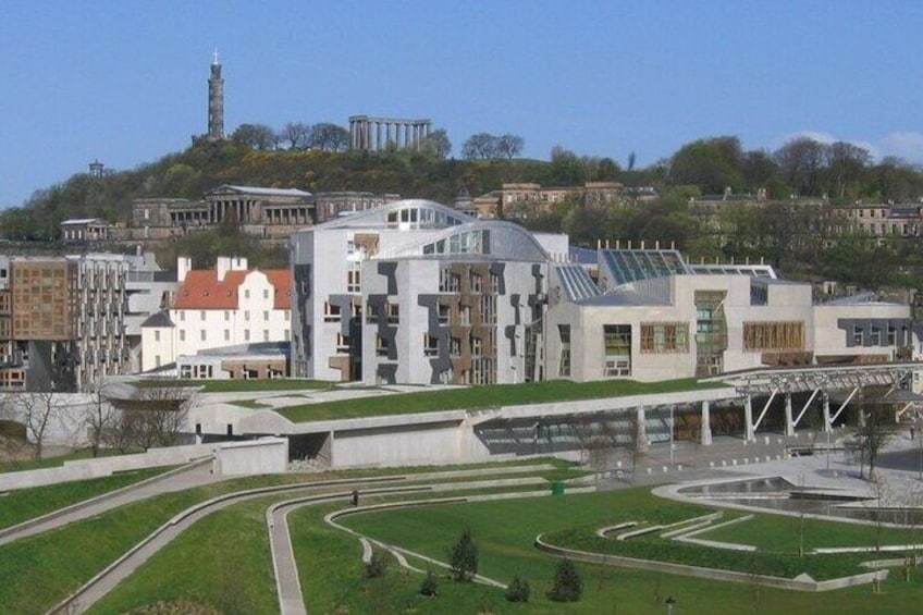 A modern building complex with a green roof, surrounded by a landscaped area with pathways and a hill with historical structures in the background. 4