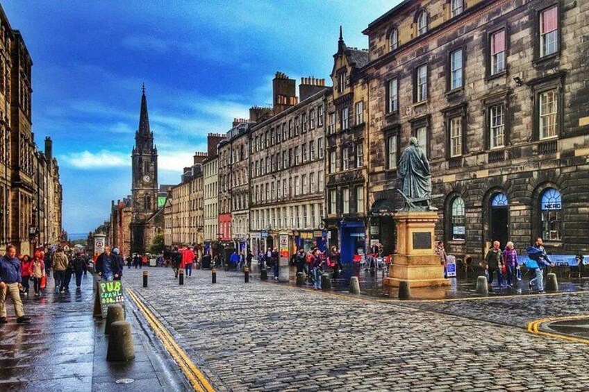 A cobblestone street lined with historic buildings, a statue, and a clock tower in the distance. 3