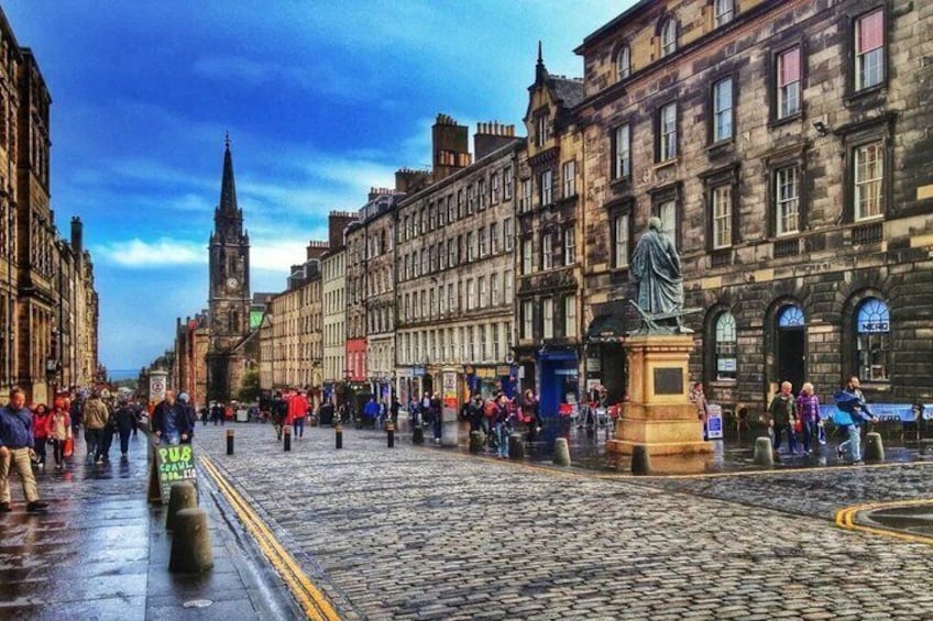 A cobblestone street lined with historic buildings, a statue, and a clock tower in the distance. 3