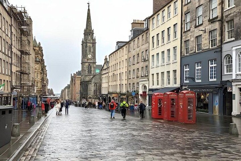 A wet cobblestone street lined with historic buildings, a church spire, and red telephone booths. 2