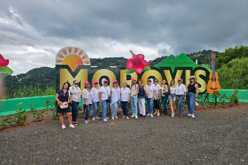 A group of people standing in front of a sign with the word 'MOROVIS' and a guitar. 2
