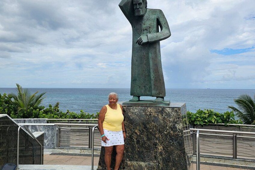 A person standing next to a statue on a platform with a view of the ocean. 5