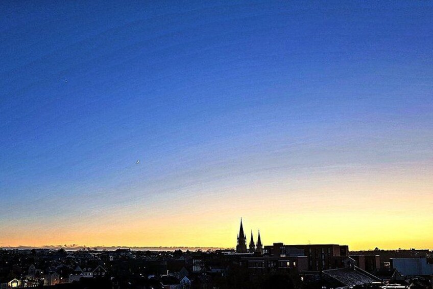 A city skyline at sunset with a clear sky, a prominent church spire, and residential buildings. 5