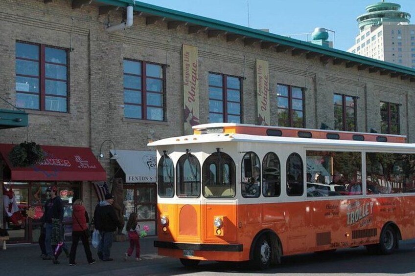 A vintage trolley bus parked in front of a brick building with storefronts. 3