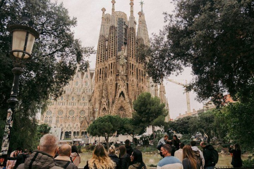 A crowd of people in front of a large, ornate building with multiple spires and intricate designs. 1