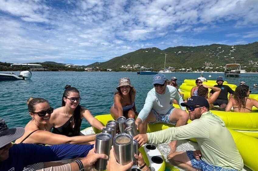 A group of people on a boat, holding drinks, with a lake and hills in the background. 2