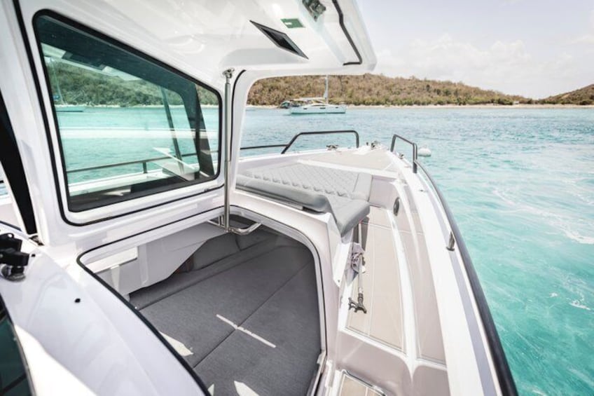 A boat's interior with a cushioned seating area and a view of a calm sea and distant shoreline. 3