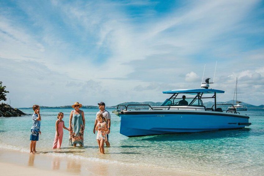 A family standing on a beach with a blue boat in the water. 1