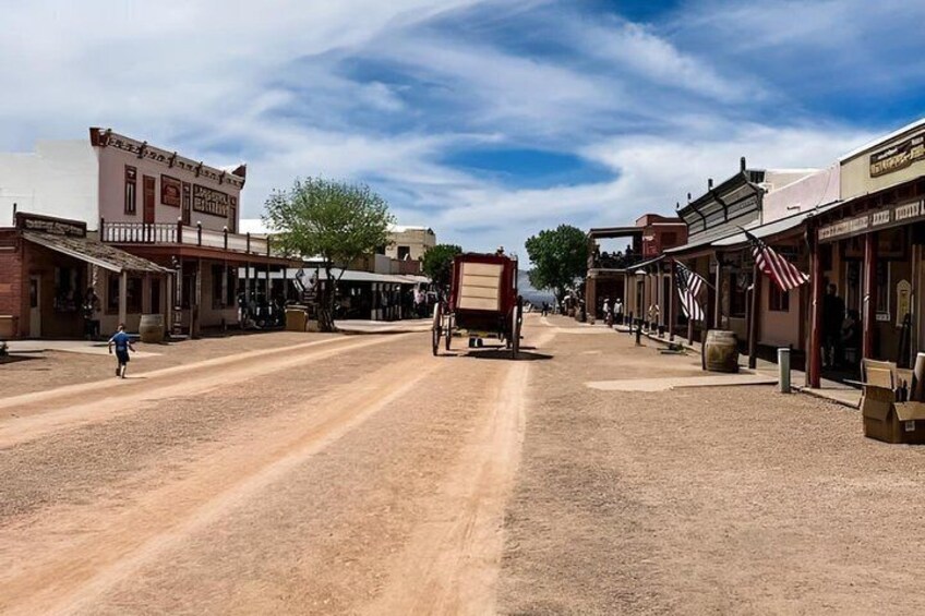 A historic town street with buildings, a horse-drawn carriage, and a clear sky. 2